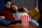 A young couple in love watching television at night romantic date night lying on the couch eating popcorn