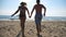 Young couple of lovers running at beach to sea holding hands. Happy girl and boy having fun together on seashore at