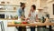 Young couple making pizza together at home. Man in apron adding mozzarella cheese on the dough and looking at woman
