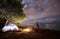 Young couple man and woman having rest at tourist tent and burning campfire on sea shore near forest