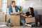 Young couple man and woman looking happy sitting on the floor in their new appartment unpacking boxes with belongings, moving