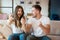 Young couple man and woman sitting on the sofa both looking joyful and satisfied, grimacing mood