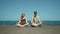 Young couple meditating sitting on pier by beach. Holidays with yoga classes