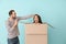 Young couple playing with box on color background. Moving into new house