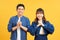 Young couple posing in a yellow background clasping hands at camera in congratulations gesture