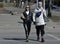 A young couple in protective masks and black gloves cross the road