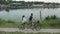 A young couple rides a tandem two-seater bike along the riverbank