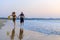 Young couple running hand in hand in the sea shore. Laughing guy and sexy slim girl jogging on the surfline. Concept of beach