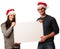 Young couple in santa hats holding blank board for advertisement