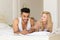 Young Couple Sit In Bed, Happy Smile Hispanic Man Frustrated Woman Using Cell Smart Phone