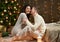 Young couple sit on floor in dark wooden interior with lights. Romantic evening and love concept. New year holiday. Christmas ligh