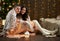 Young couple sit on floor in dark wooden interior with lights. Romantic evening and love concept. New year holiday. Christmas ligh