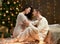 Young couple sit on floor in dark wooden interior with lights. Romantic evening and love concept. New year holiday. Christmas ligh