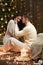 Young couple sit on floor in dark wooden interior with lights. Romantic evening and love concept. New year holiday. Christmas ligh