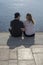 Young couple sit in sunshine watch water glitter on stone pier