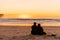 Young couple sitting on the beach watching golden sunset