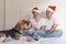 young couple sitting on bed with christmas santa hats having fun with their dog. Presents on bed. Home, indoors. Xmas concept