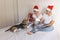 young couple sitting on bed with christmas santa hats having fun with their dog. Presents on bed. Home, indoors. Xmas concept