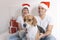 young couple sitting on bed with christmas santa hats having fun with their dog. Presents on bed. Home, indoors. Xmas concept