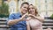 Young couple sitting close to each other putting up finger-shaped heart, kissing