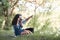 Young couple sitting on the grass in the forest, taking photos and looking on sunset, summer nature, bright sunlight, shadows and