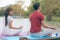 Young couple sitting on the mat beside the lake and doing meditation together