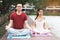 Young couple sitting on the mat beside the lake and doing meditation together