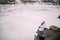 Young couple is sitting at rock, embracing and looking at frozen lake.