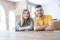 Young couple sitting on the table movinto to new home with carboard boxes behind them happy face smiling with crossed arms looking