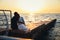 Young couple sitting and watching the sunrise at the beach, back view, seashore summer beach at yellow blue morning horizon sea