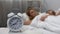 Young couple sleeping in bed with ringing alarm clock on table, sleep biorhythms