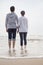 Young couple standing and holding hands on the beach and looking out to sea