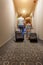 Young couple standing at hotel corridor upon arrival, looking for room, holding suitcases.