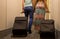 Young couple standing at hotel corridor upon arrival, looking for room, holding suitcases