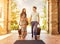 Young couple standing at hotel corridor upon arrival, looking for room, holding suitcases