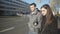 Young couple standing near road, man unconfidently catching taxi, hitchhiking