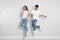 Young couple in stylish jeans jumping near wall