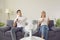 Young couple suffering from hot summer weather and sitting on sofa with electric fan