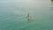 Young couple sup surfing on tranquil sea surface against coastline on horizon