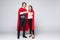 Young couple of superheroes in costumes standing with hands to hands and looking at camera isolated on white background