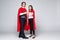 Young couple of superheroes in costumes standing with hands to hands and looking at camera isolated on white background