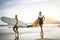 Young couple of surfers running with surfboards on the beach at sunset - Happy lovers going to surf together