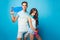 Young couple of teenagers posing on blue background in studio. They wear T-shirts, jeans shorts, hold skateboards and