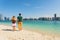 Young couple of tourists holding hands on beach looking at the modern buildings from Abu Dhabi. Honeymoon excursion and summer tra