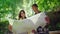 A young couple of tourists looking at a map. They stand in the rays of the sun in the forest near the waterfall