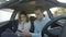 Young couple using smart phones in car and man shows phone to girlfriend and she is shocked -