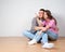 Young couple visualizing the decor of their new home sitting on the bare wooden floor pointing out and discussing placement of fur