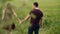 Young couple walking in an oat field. They hold hands, womans hair sway in the air as she turns head. Backview, slow mo