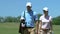 Young couple walking to next hole on golf course, man carrying golf bag, hobby