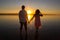 Young couple is walking in the water on summer beach. Sunset over the sea.Two silhouettes against the sun. Just married couple